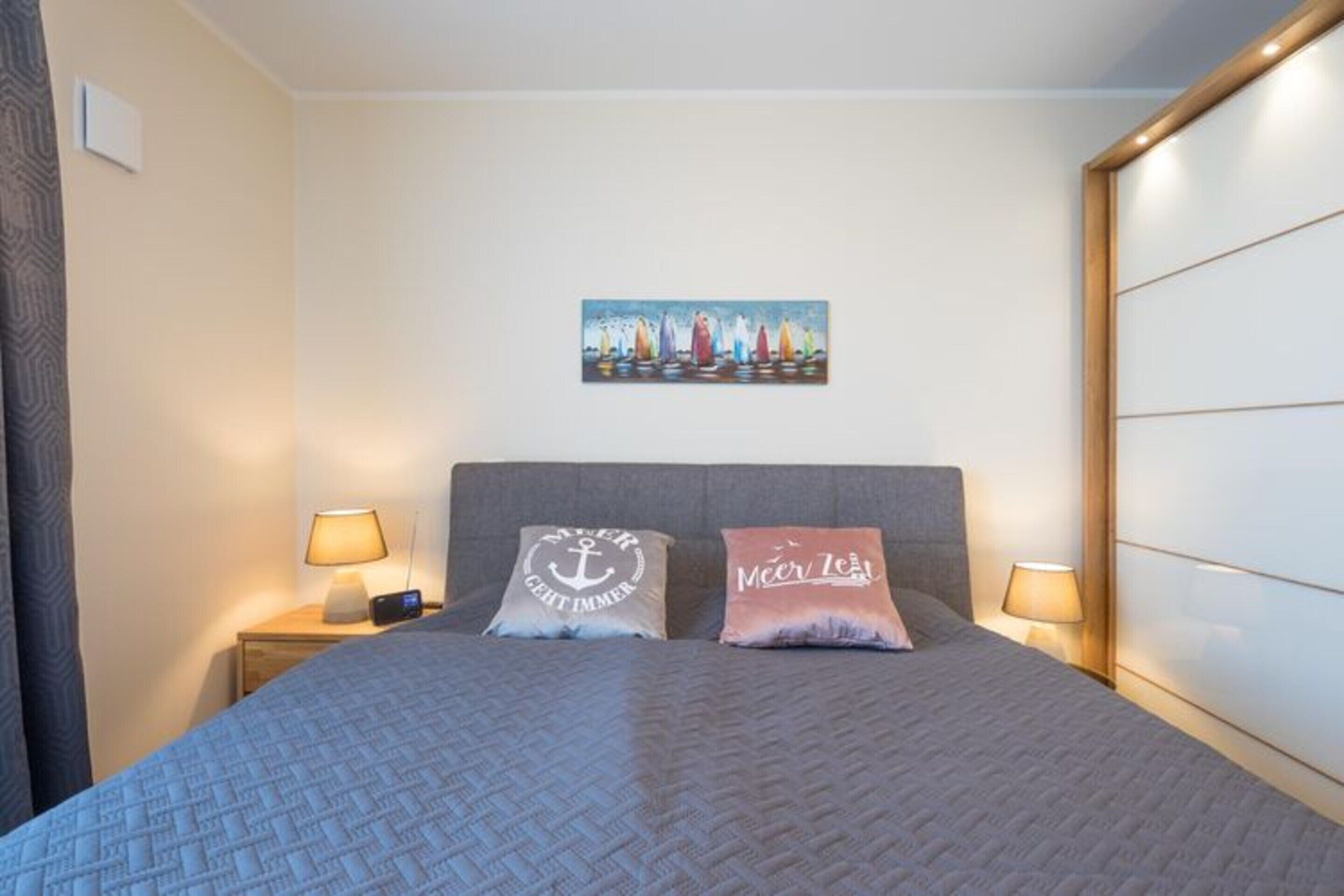 Hotelkamer met een bed, twee nachtkastjes met lampen, een aan de muur hangend schilderij en twee kussens met tekst.