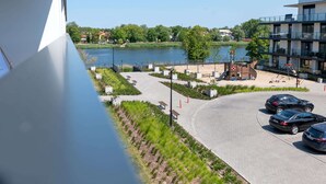 Näkymä järvenrantapuistoon, jossa on leikkikenttä, penkkejä ja pysäköintialue autoineen.