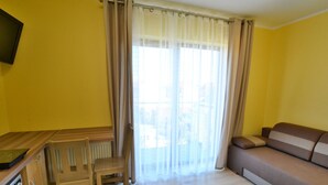 A room with yellow walls, a wooden desk with a chair, a sofa, and a television mounted on the wall. - 2-person Studio in the Attic, Sarbinowo (Mielno)