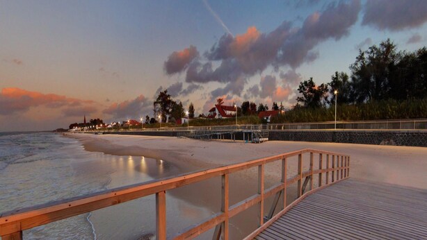 A wooden boardwalk leading to a beach with a view of houses and trees in the background. - 2-person Studio in the Attic, Sarbinowo (Mielno)