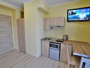 Una cocina compacta con armarios de madera, horno empotrado, lavavajillas y un televisor de pantalla plana montado en la pared.