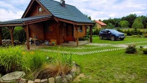 A wooden cabin with a sloped roof, a covered porch, and a car parked in the driveway. - Holiday Home in Kolczewo for Nature Lovers (gmina Wolin)