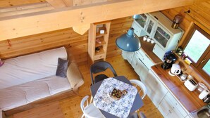 A compact wooden cabin with a bed, a dining table with chairs, a kitchenette, and a small window. - Holiday Home in Kolczewo for Nature Lovers (gmina Wolin)