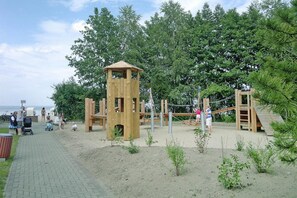 Explore the playground's lookout tower and climbing elements amidst lush greenery and a serene body of water.