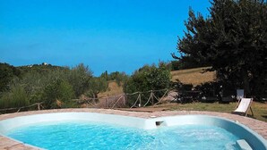 Une piscine rectangulaire bordée de briques, entourée d’une pelouse et d’arbres.