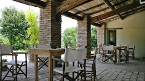 Une terrasse extérieure avec des tables et des chaises en bois rustique, des piliers en briques et un plafond couvert.