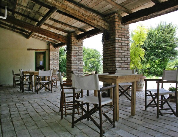 Une terrasse extérieure avec des tables et des chaises en bois rustique, des piliers en briques et une vue sur la verdure.