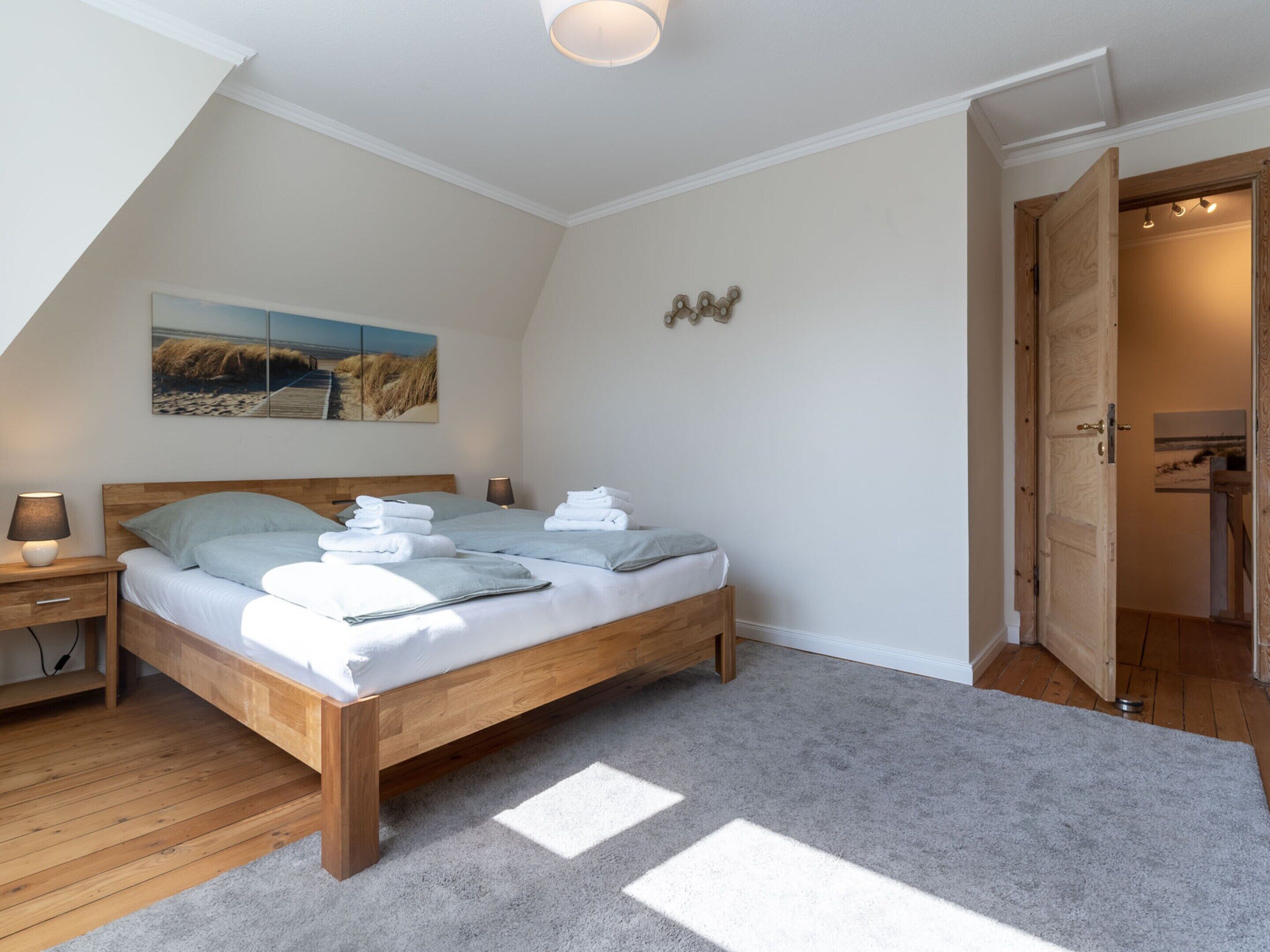 A bedroom with a wooden bed, a nightstand, a lamp, and a painting on the wall.
