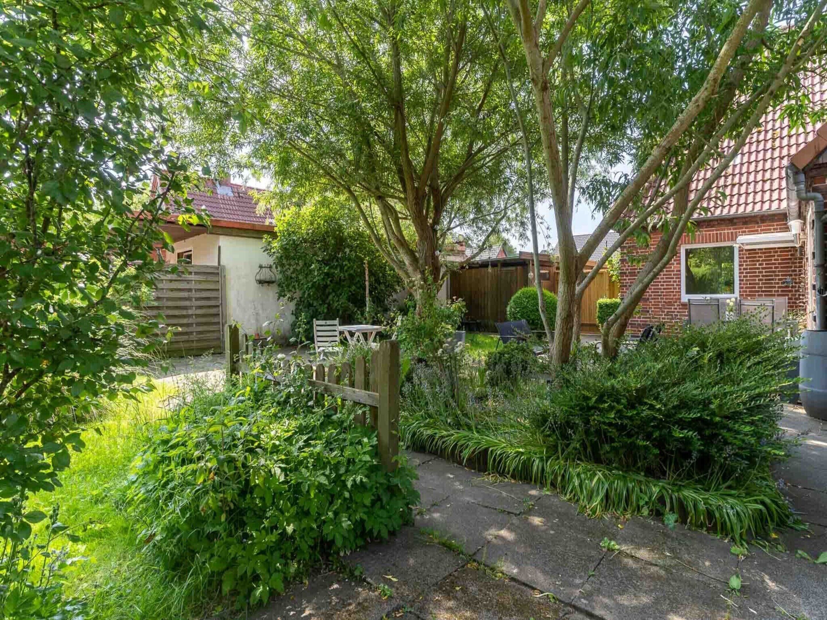 A garden with a wooden fence, a paved path, and a brick house with a tiled roof.