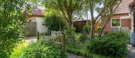 A garden with a wooden fence, a paved path, and a brick house with a tiled roof.