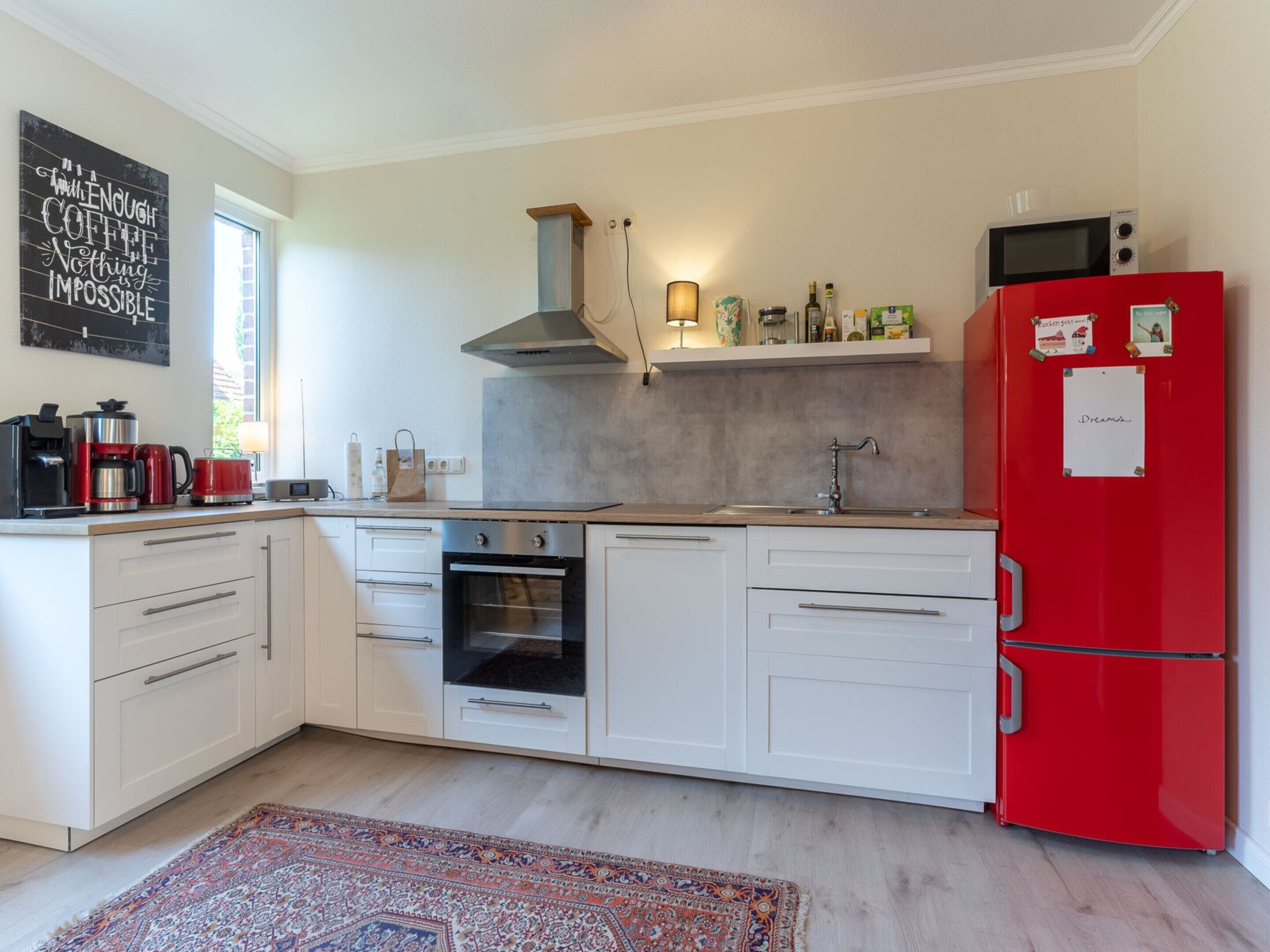 A modern kitchen with white cabinets, a red refrigerator, a built-in oven, and a coffee maker.