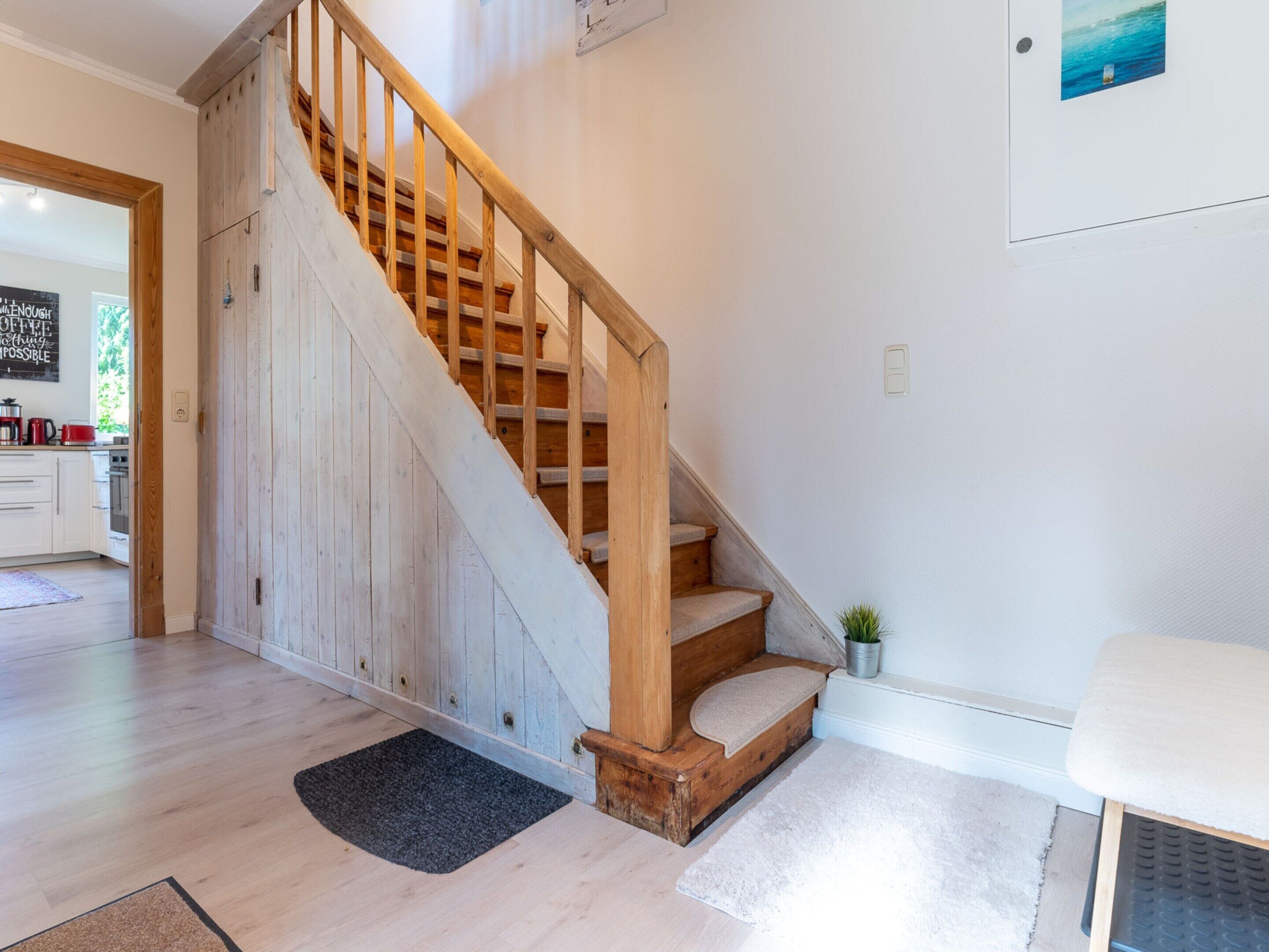 A wooden staircase with a bench at the bottom, leading to a kitchen area with white cabinets and a blackboard on the wall.