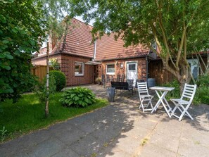 A brick house with a tiled roof, a patio with outdoor furniture, and a garden area.