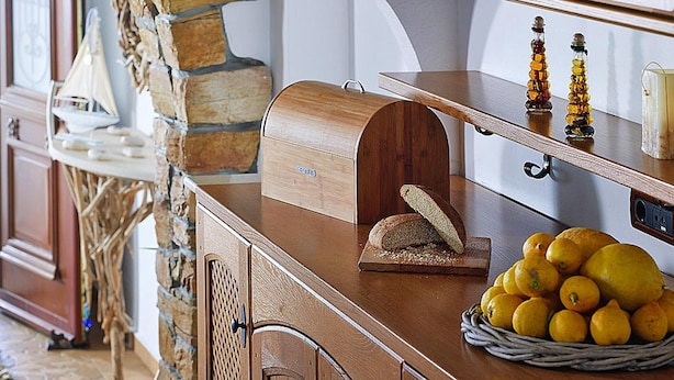A kitchen counter with a wooden bread box, a loaf of bread, a basket of lemons, and a stone wall. - Detached Villa With Seaview in Charaki (Rhodes)