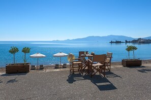 Eine Strandterrasse mit Tischen, Stühlen und Sonnenschirmen mit Blick auf ruhiges Wasser.