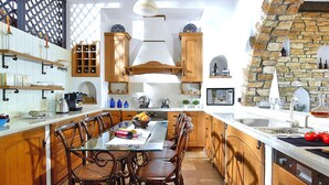 A kitchen with wooden cabinets, a dining table with chairs, a stone arch, and a hanging light fixture. - Detached Villa With Seaview in Charaki (Rhodes)