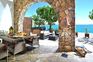Eine Terrassengaststätte mit Korbmöbeln, einem Steinbogen und Blick aufs Meer.