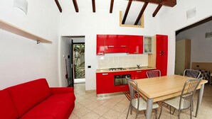 A compact kitchen with red cabinets, a wooden dining table, and a red sofa. - Apartment in Castellaro With Balcony (Casanova Lerrone)