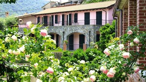 A pink building with a stone facade and arched windows, surrounded by lush greenery and roses. - Apartment in Castellaro With Balcony (Casanova Lerrone)