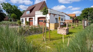 A house with a sloped roof, a garage, and a garden area with tall grass and a brick structure. - Holiday Home in Tating (Tating)