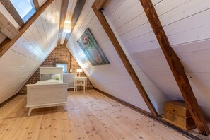 Ein Schlafzimmer im Loft-Stil mit schrägem Dach, Holzbalken, einem weißen Bett, einer kleinen Kommode und einem Heizkörper.