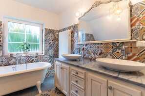 Ein Badezimmer mit freistehender Badewanne, zwei Waschbecken und einem großen Spiegel.