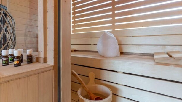 A wooden sauna with a bench, a towel, and bottles of essential oils on a shelf. - Holiday Home in Tating (Tating)