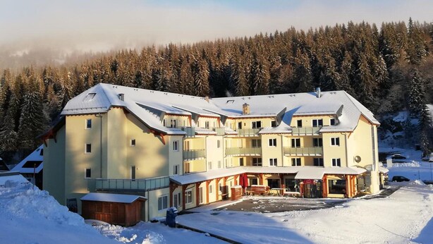 Un hôtel à plusieurs étages, dont le toit est recouvert de neige, et qui est entouré d’une forêt.