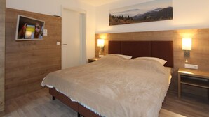 Une chambre avec un grand lit, une tête de lit en bois, deux tables de chevet avec des lampes, un tableau au mur et une porte.