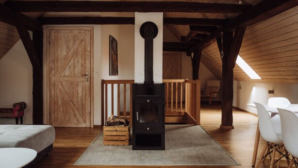 A cozy room with a wooden ceiling, a black wood stove, a white door, and a dining area with white chairs.