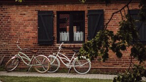 A brick building with two windows and a bicycle parked in front.