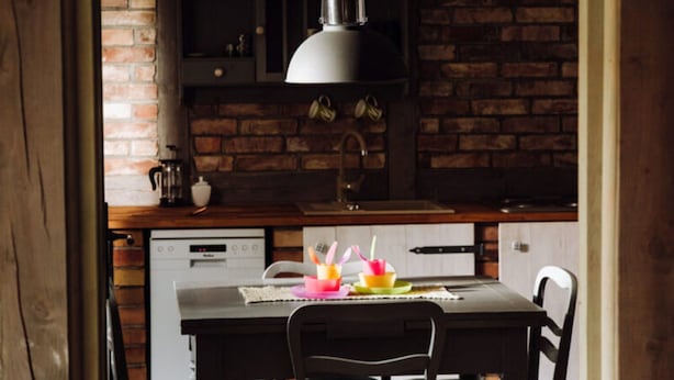 A kitchen with a brick wall, a hanging light fixture, a dishwasher, and a table with colorful cups. - Apartment in Gronowo Near Lake Siecino (Zlocieniec)