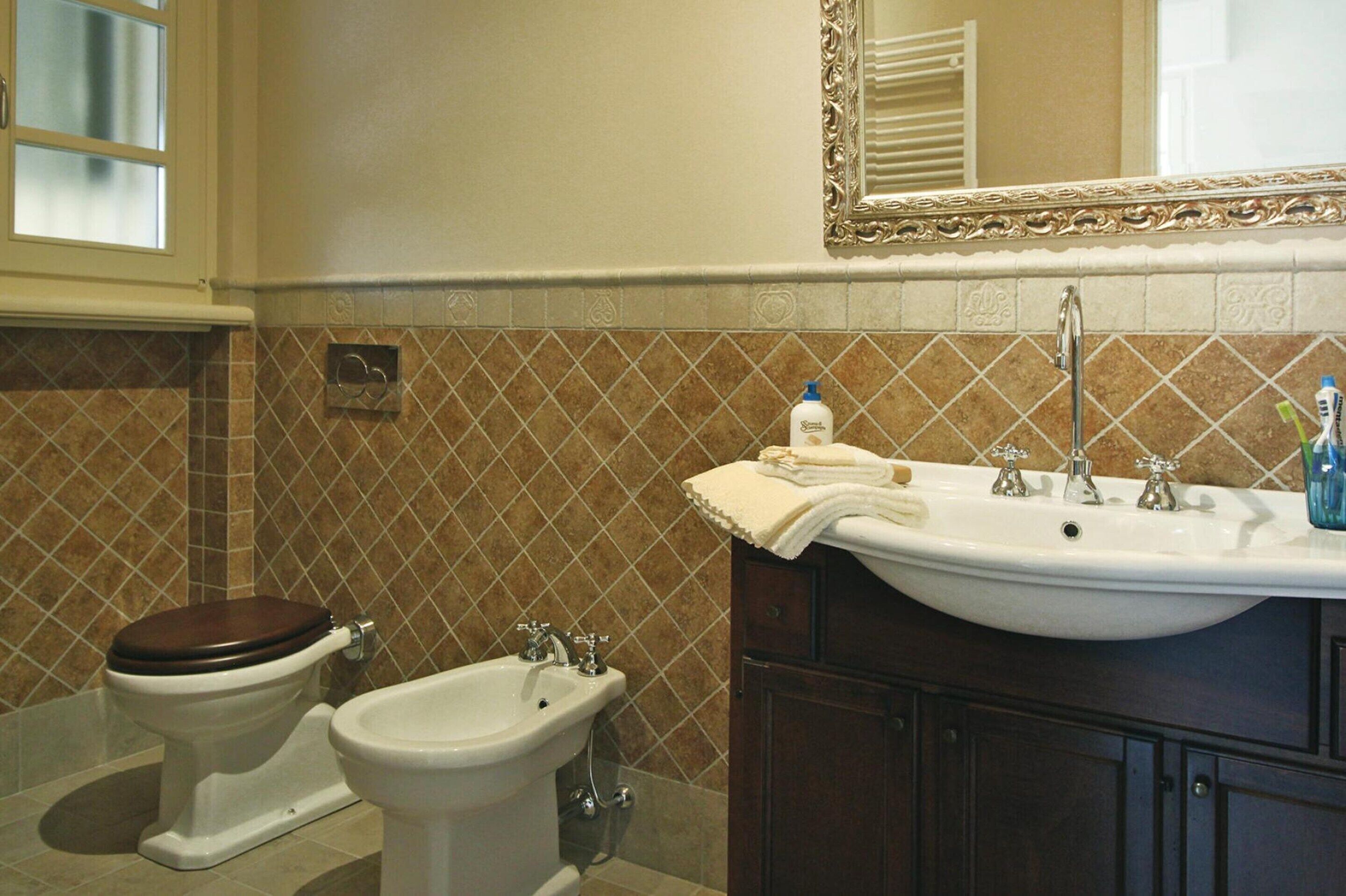A bathroom with a toilet, bidet, sink, and mirror.