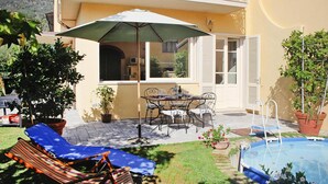 A patio with a pool, lounge chairs, a table with chairs, and potted plants. - Villa in Camaiore Near Sandy Beaches (Camaiore)