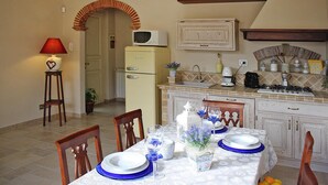 A dining area with a table set for four, a microwave, a refrigerator, and a kitchen counter with various appliances and a wine rack. - Villa in Camaiore Near Sandy Beaches (Camaiore)
