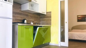 A compact kitchen with a microwave, a stove, and a sink. There is a bed visible through an open door in the adjacent room. - Holiday Villa Apartment in Imperia (Imperia)