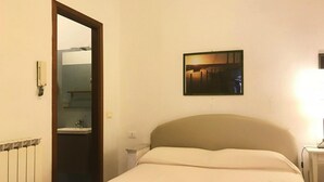 A hotel room with a bed, a bedside table, a nightstand, a wall-mounted picture, and a door leading to a bathroom. - Holiday Villa Apartment in Imperia (Imperia)