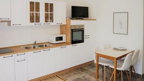 Une cuisine compacte avec des meubles blancs, un four à micro-ondes, un four traditionnel, un évier et une table à manger avec des chaises.