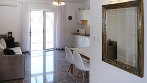 Un salon avec un canapé, une table à manger avec des chaises, un coin cuisine équipé d’un four à micro-ondes et un grand miroir au mur.