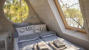 Een gezellige slaapkamer met een schuine kap, een rond raam en een bed met 'Mr. & Mrs.' kussens.