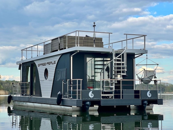 A houseboat with a covered deck, a staircase, and a small outdoor area with a hanging chair. - Houseboat on the Dahme (Königs Wusterhausen)