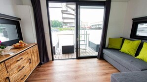 En moderne stue med et træskab, en grå sofa med grønne puder og en skydedør af glas, der fører til en udendørs balkon.