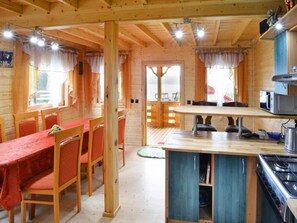 A wooden cabin interior with a dining area, kitchen, and large windows. - Wooden House by Ostrowieckie Lake With Beach (Malechowo)