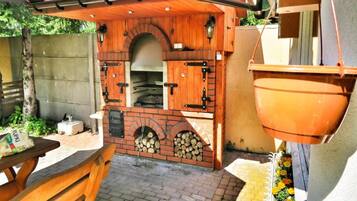 An outdoor kitchen area with a brick oven, wooden cabinets, and a hanging pot rack.