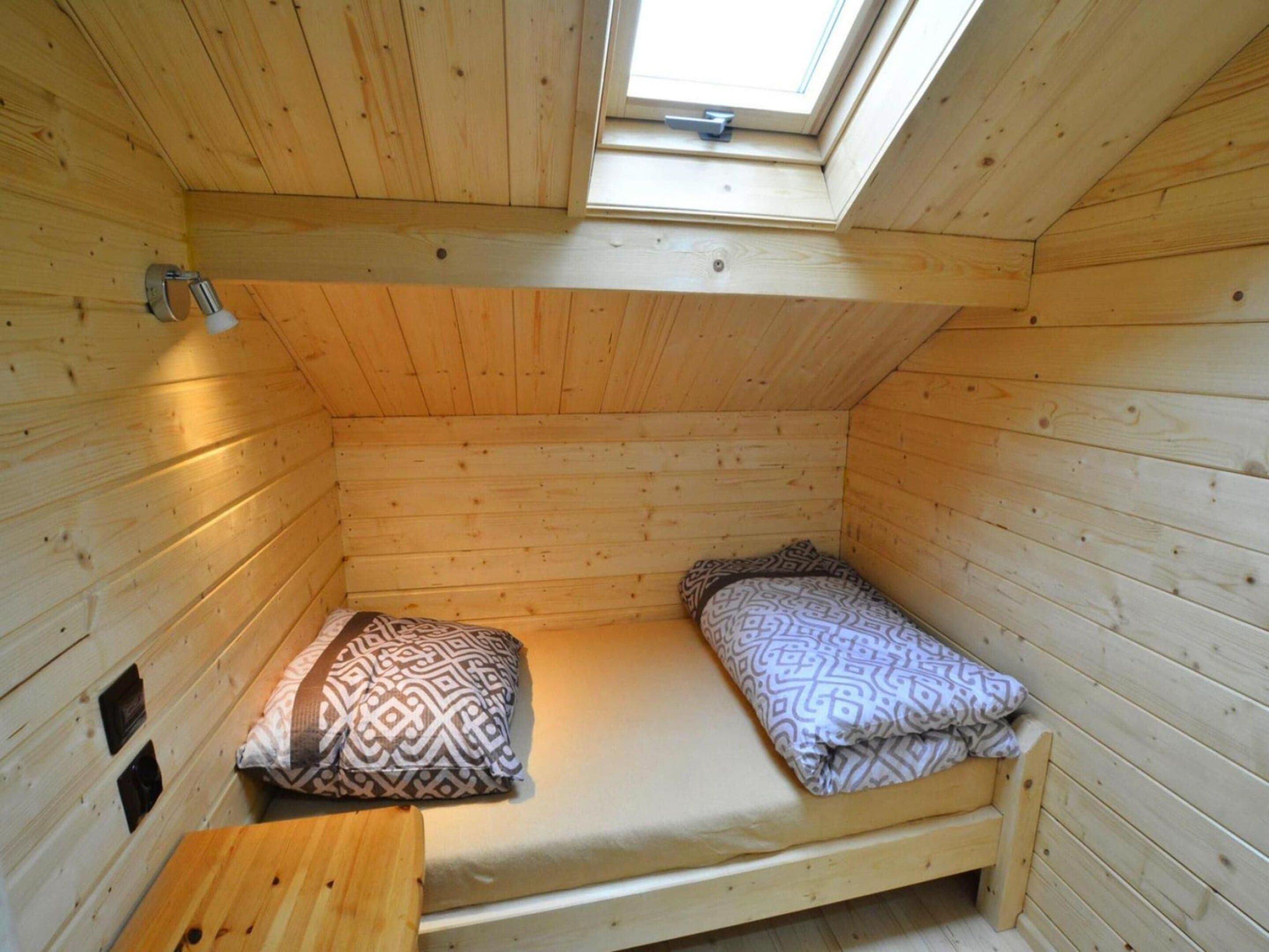 A small, single-occupancy room with a sloped ceiling and a skylight, featuring a bed with patterned bedding and a wooden bench.