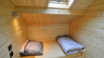 A small, single-occupancy room with a sloped ceiling and a skylight, featuring a bed with patterned bedding and a wooden bench.