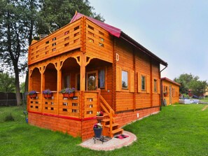 A wooden cabin with a porch, a staircase, and a small garden area. - Wooden House by Ostrowieckie Lake With Beach (Malechowo)