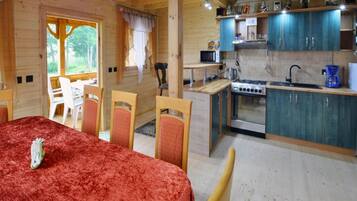 A cozy cabin interior with a dining area, kitchen, and a window overlooking greenery.