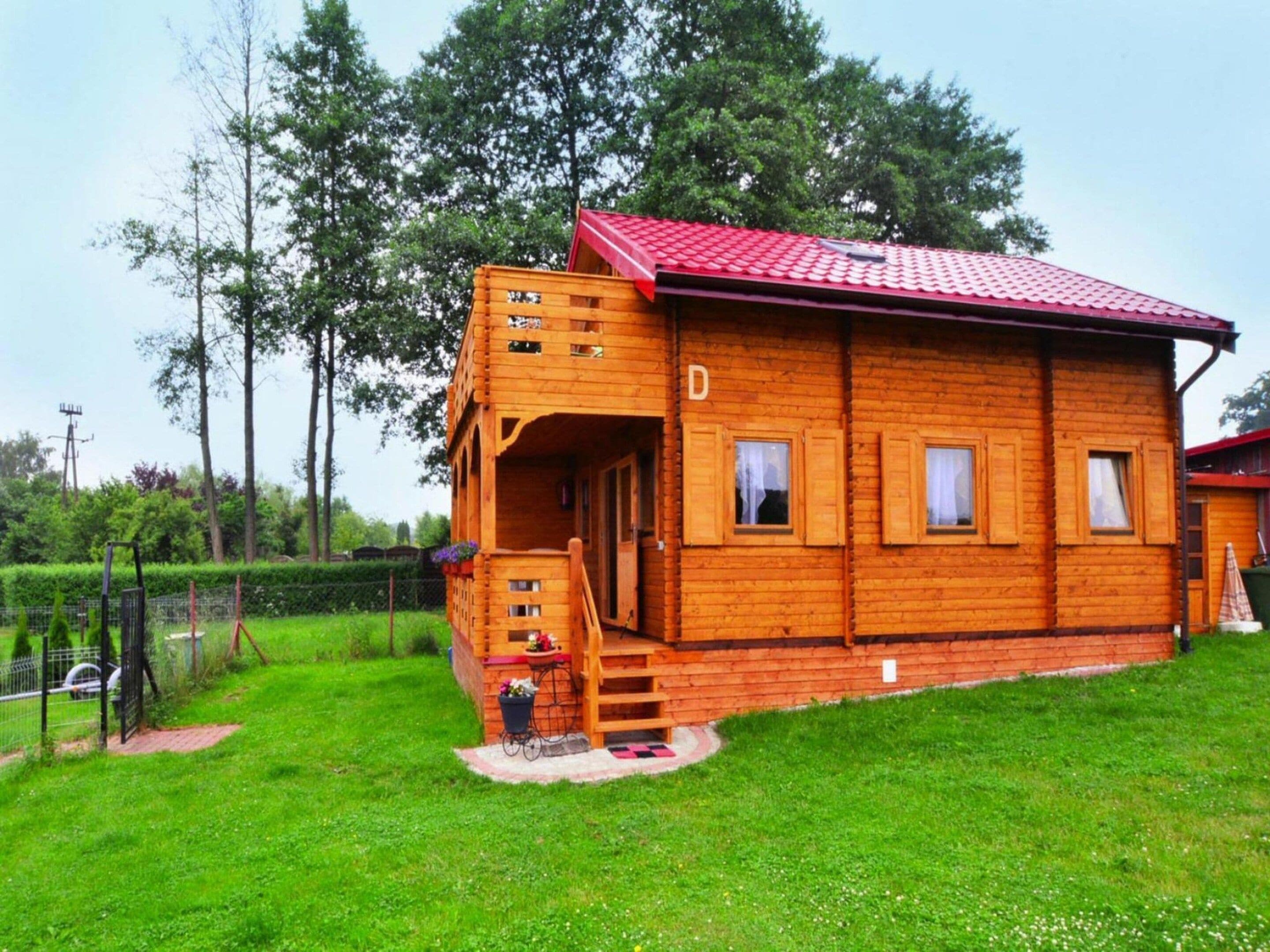 A wooden cabin with a red roof, a porch, and a fenced yard.