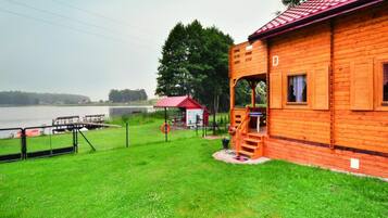 A wooden cabin with a red roof, a small porch, and a view of a lake.